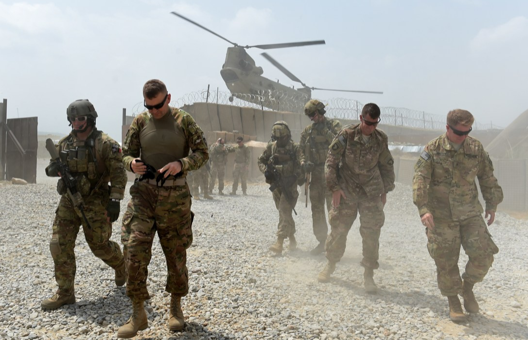 US army soldiers walk as a NATO helicopter flies overhead at coalition force Forward Operating Base