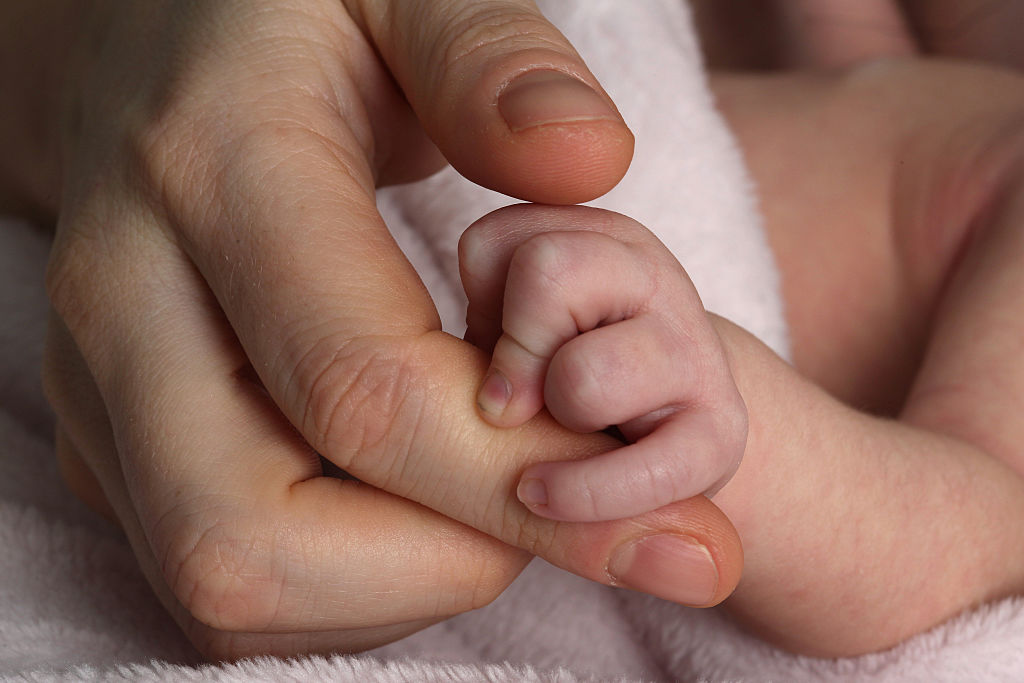 three week old baby girl holds her mothers finger