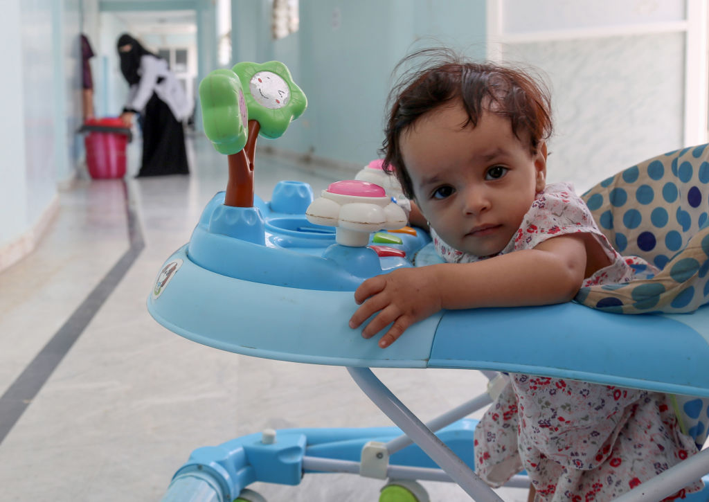 A female toddler looks at the camera while sitting in her babywalker