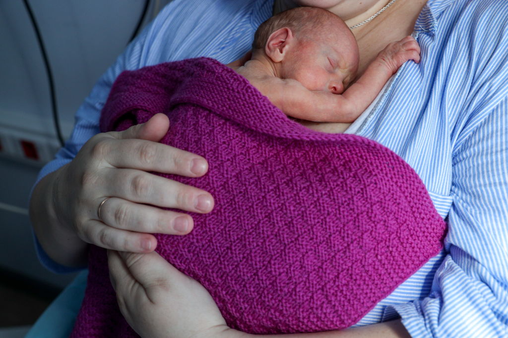 A newborn baby lays on a woman's chest covered in a pink blanket.