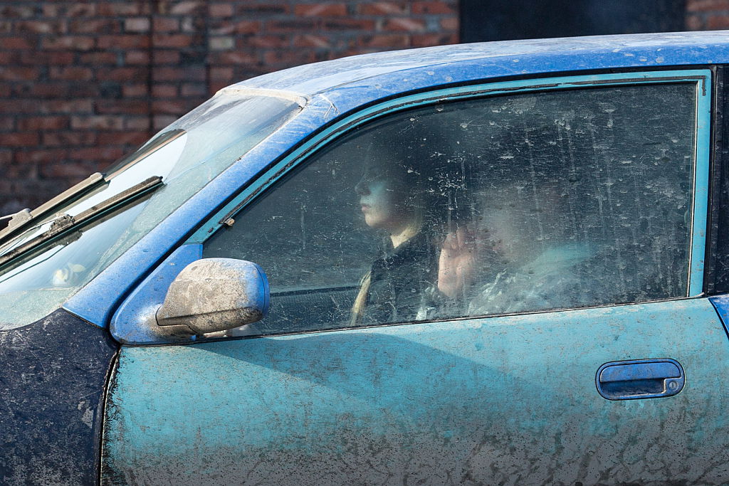 Two people ride in a car that is covered in dirt.