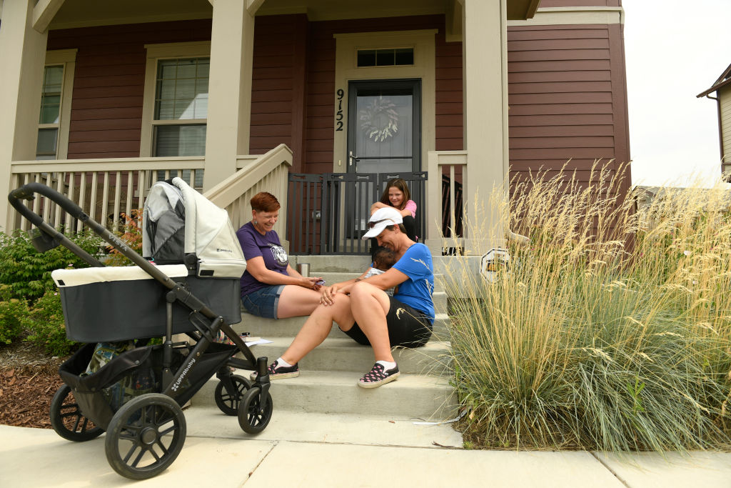 Women gather on front porch steps to admire a baby