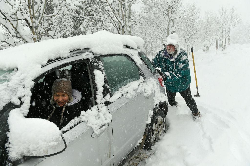 A man assists a woman while she's stuck in her car in a snowstorm
