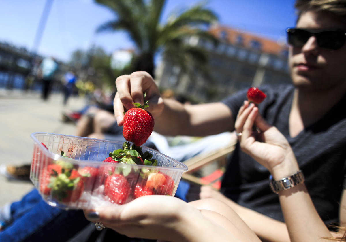 A couple eat strawberries sitting on a river on a sunny day in Berlin