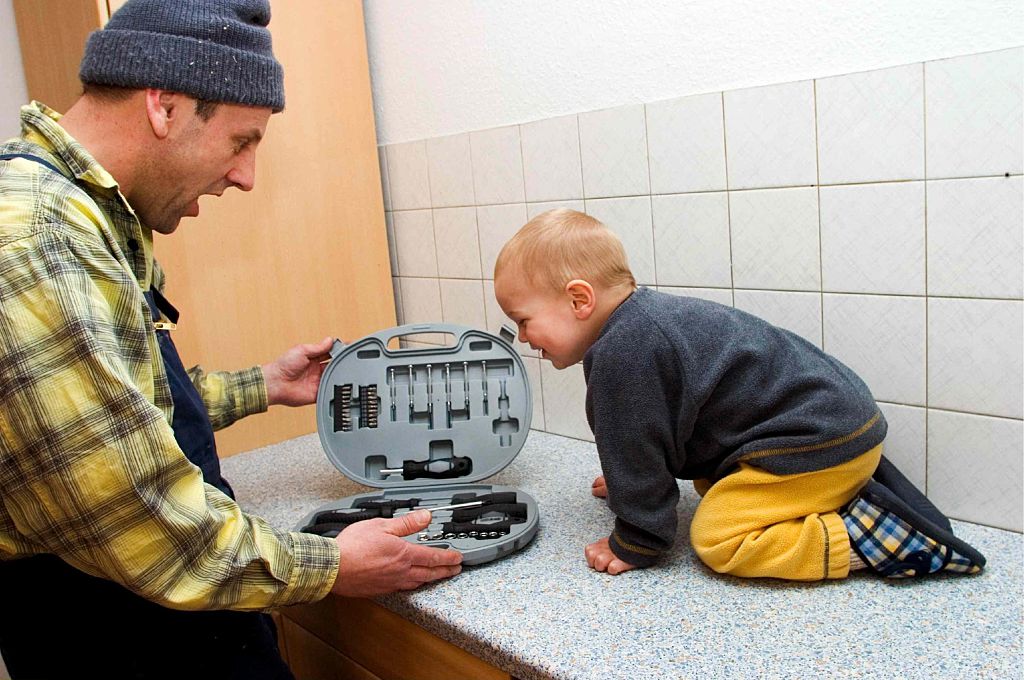 A man and toddler boy look into a tool set