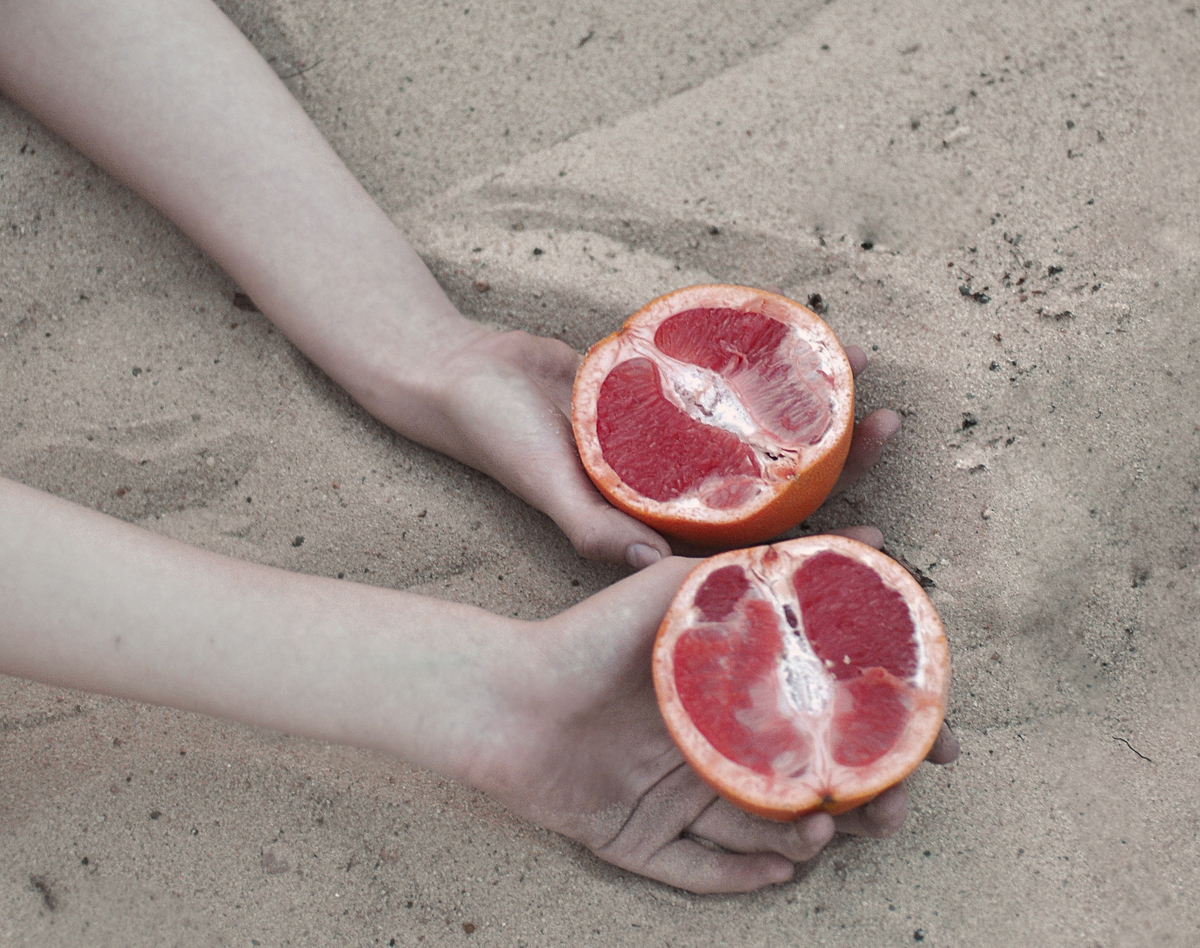 Person holds sliced grapefruit in the sand