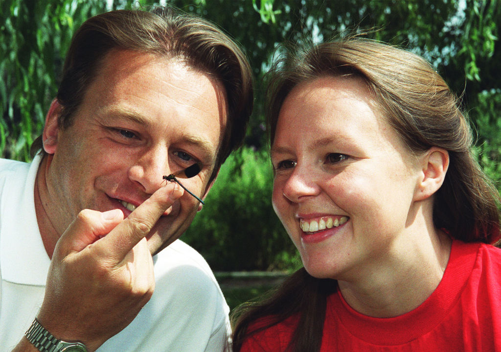 A man and woman observe a dragonfly as it sits on the man's finger.