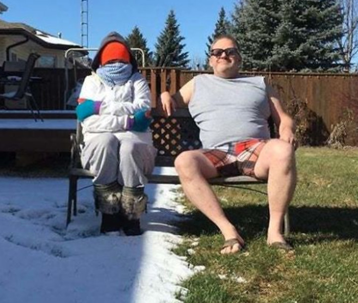 Two people next to each other are dressed and sitting in opposite weather (snowy vs. sunny and grassy)