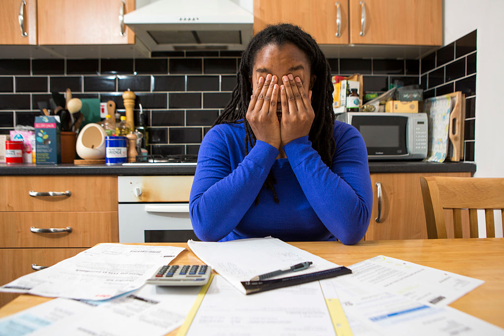 A young lady sits at her kitchen table at home checking over the household bills. 