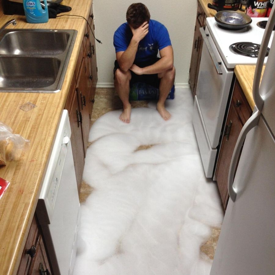man sitting in kitchen with soap on the floor after dishwasher overflowed