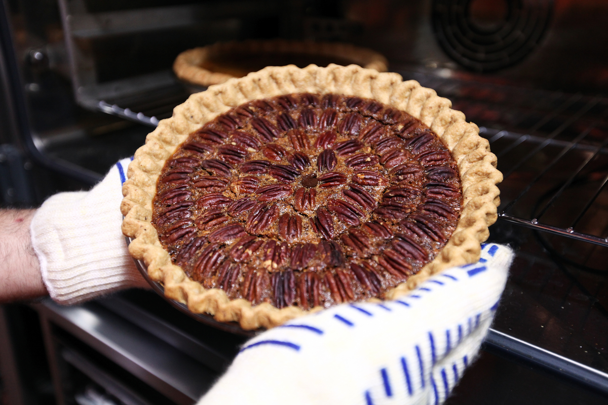 Baker pulls a pecan pie out of an oven.