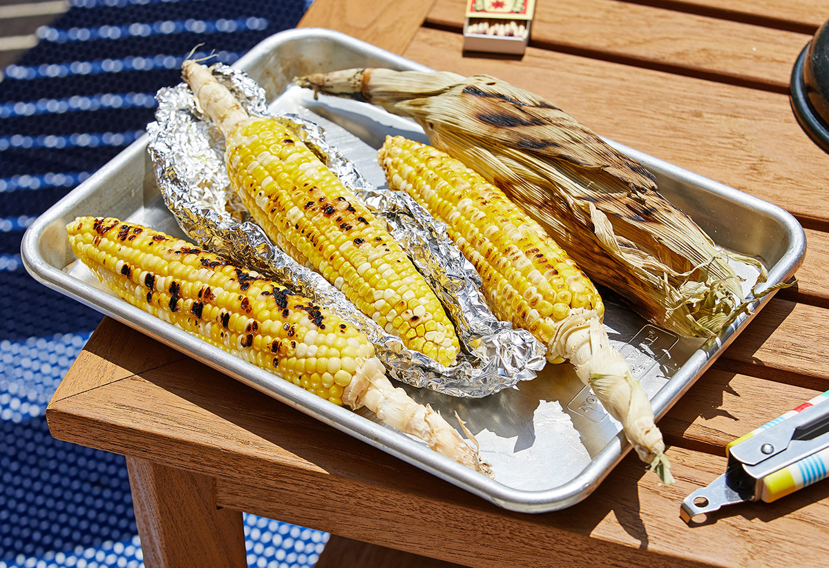 Grilled corn on the cob rests on a pan outdoors.