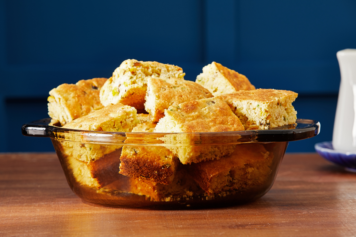Cornbread slices fill a bowl in front of a blue backdrop.