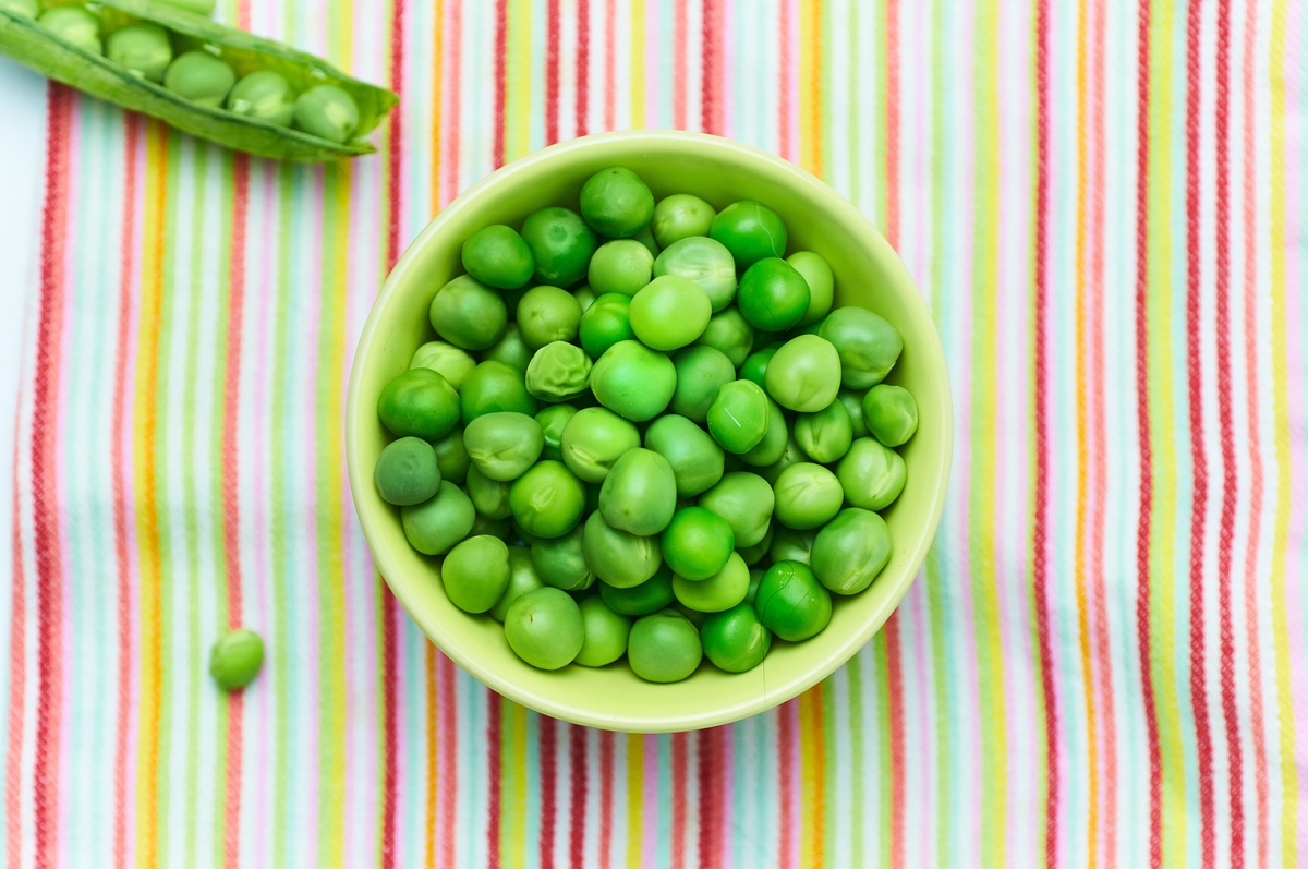 A bowl on a striped tablecloth holds peas.