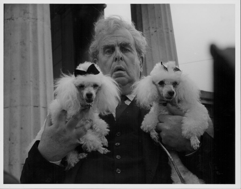 A man looks distraught as he holds a small poodle in each hand.