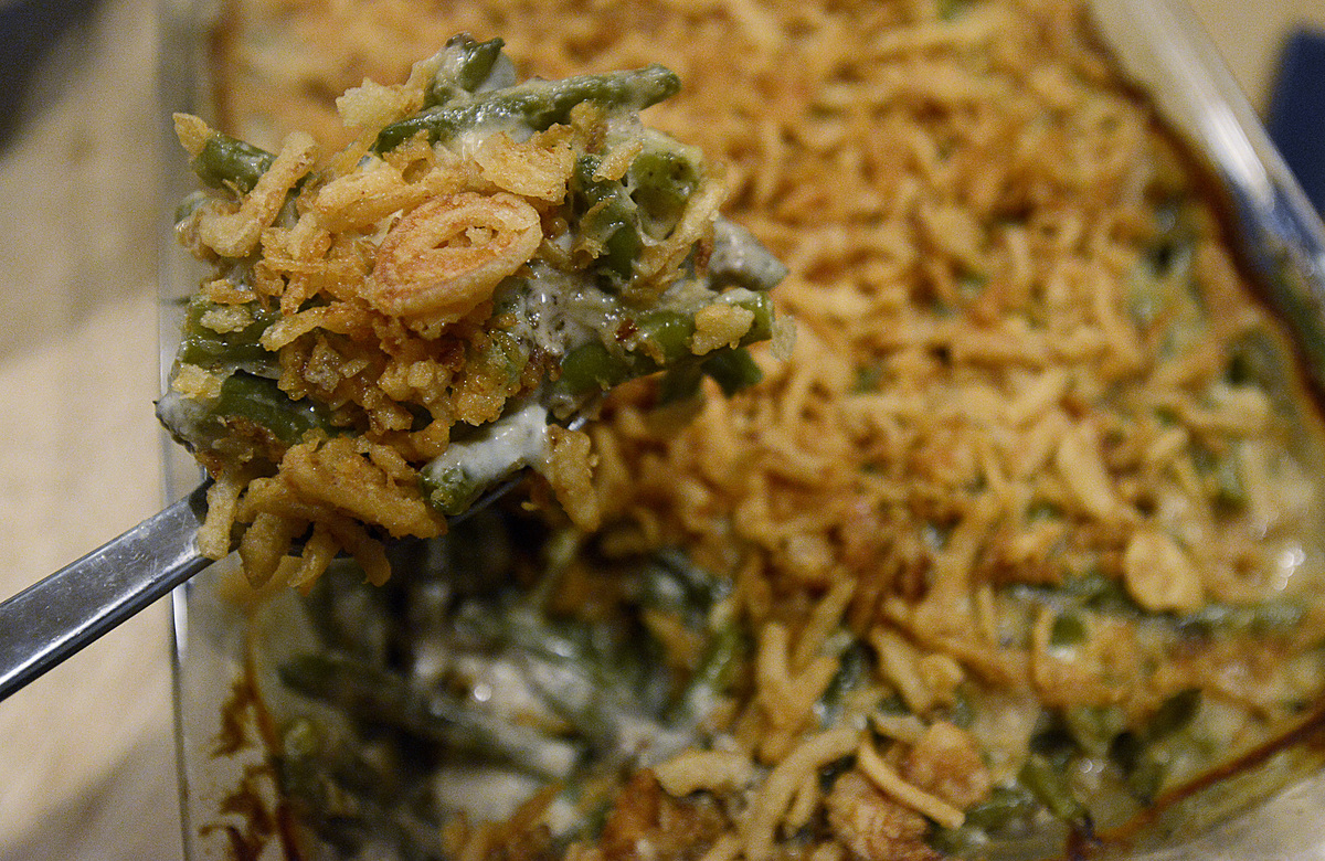 Person removes a spoonful of green bean casserole from a pan.