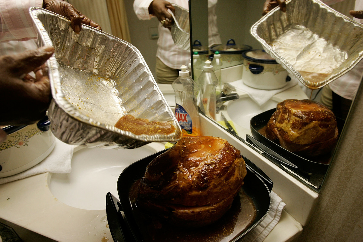 Kathy Curry of New Orleans puts glaze on a ham as she prepares her Thanksgiving dinner in the bathroom of her hotel room.