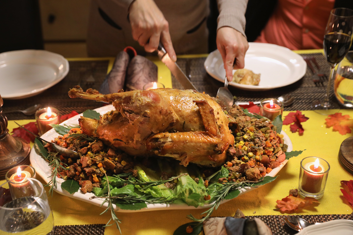 A person carves the Thanksgiving turkey on a dinner table. 
