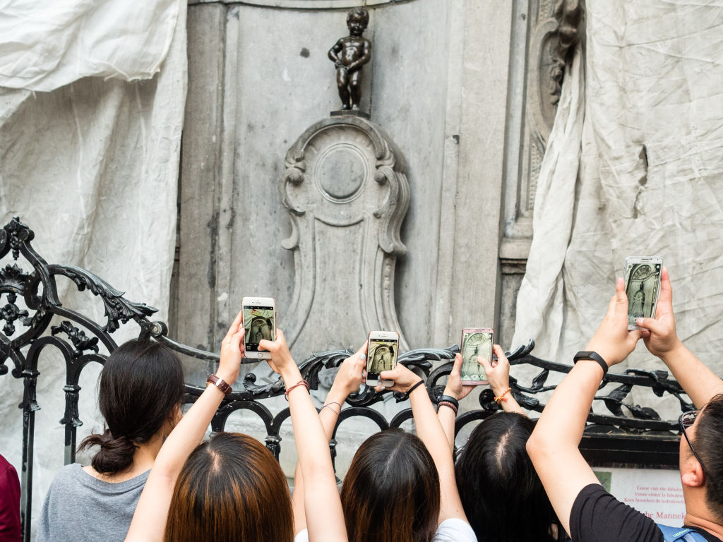 Manneken Pis Is A Tiny Statue Behind A Wall Of Tourists