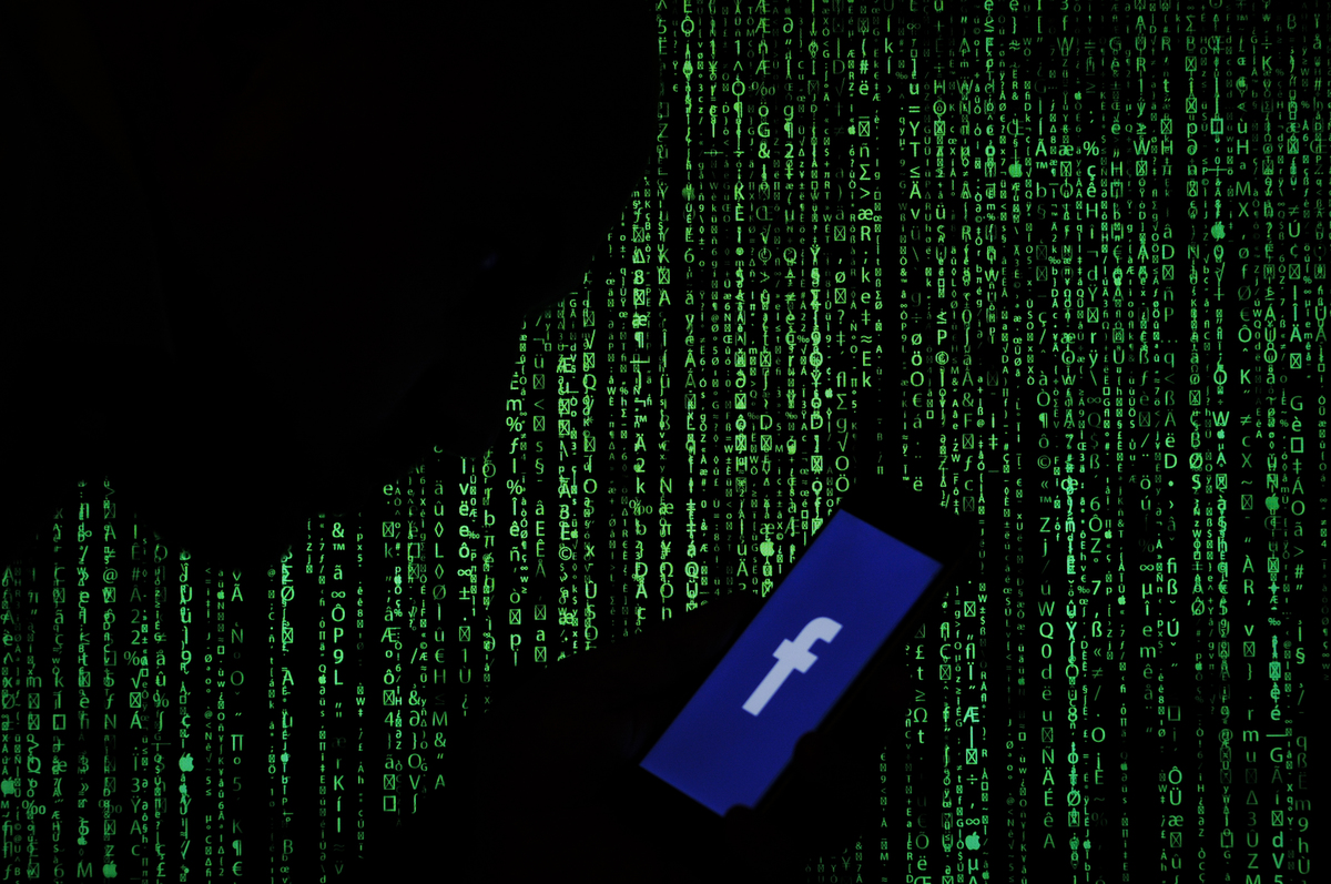 A Facebook logo is seen on a smartphone with computer numbers in the background.
