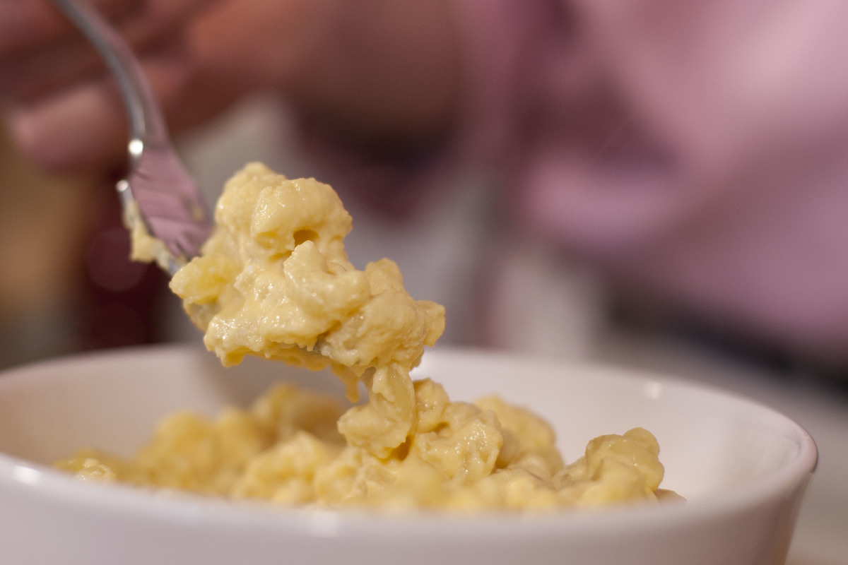 A close-up shows someone eating creamy mac and cheese with a fork.