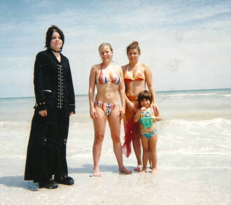 a family picture on a beach, one of them is goth