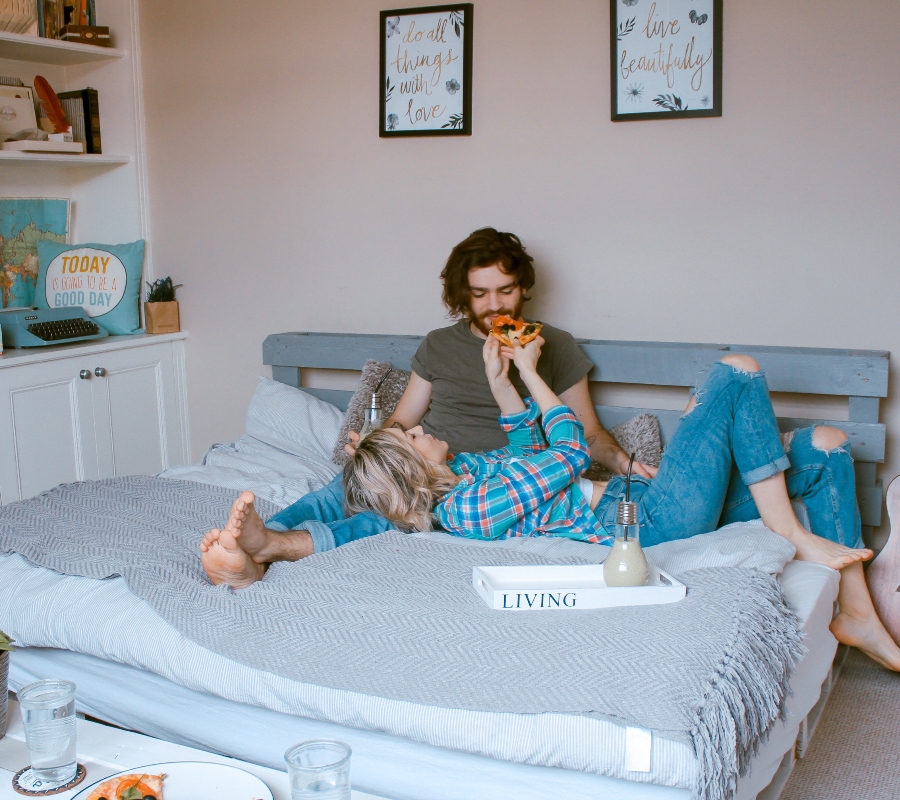 a couple lying in bed eating pizza