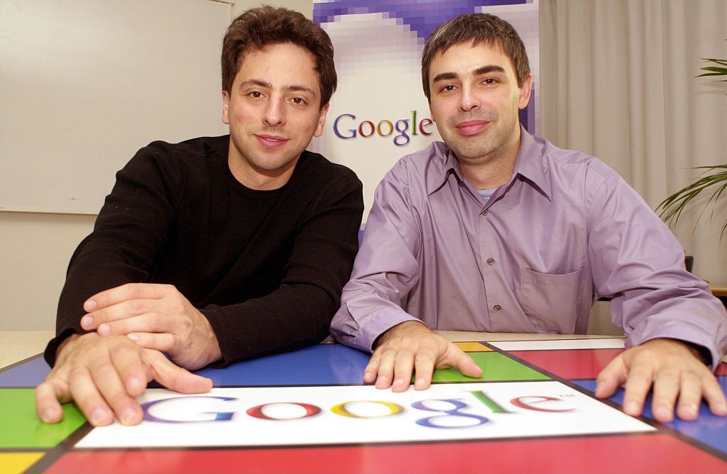larry page and sergey brin sitting at a table with the google logo
