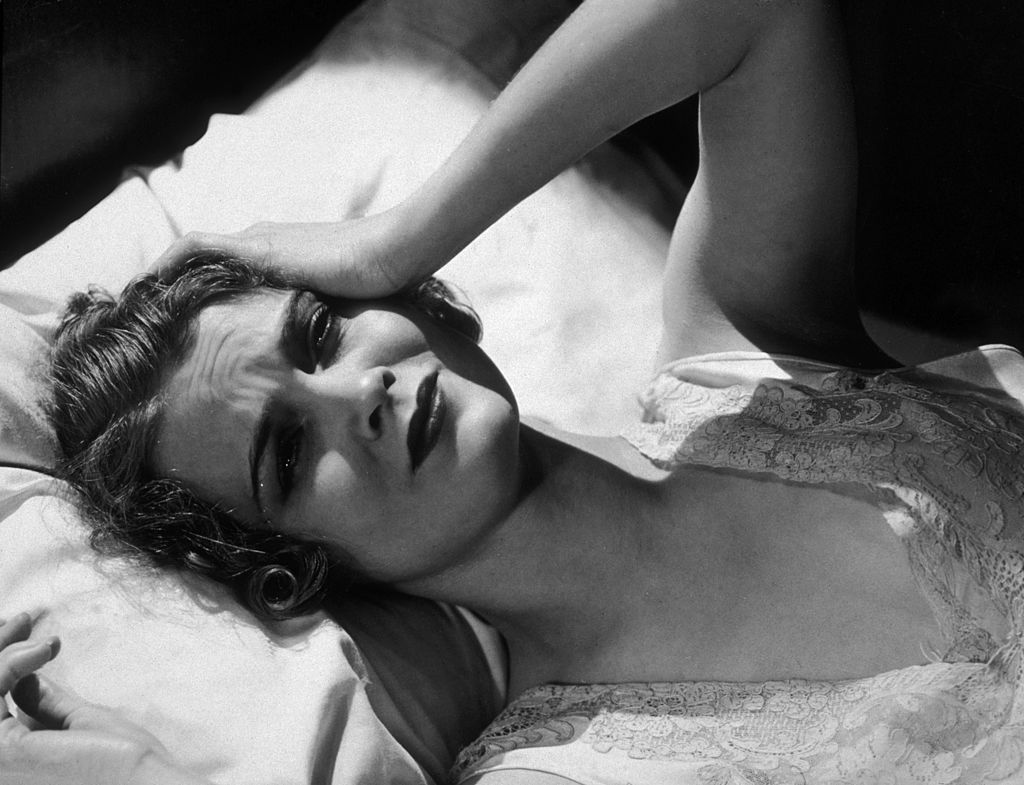 A woman lays in bed and looks unwell.
