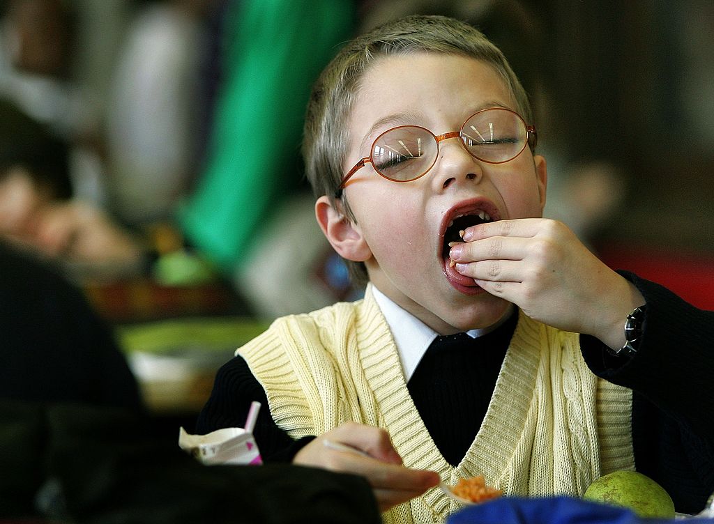 A young boy closes his eyes while placing food into his mouth.