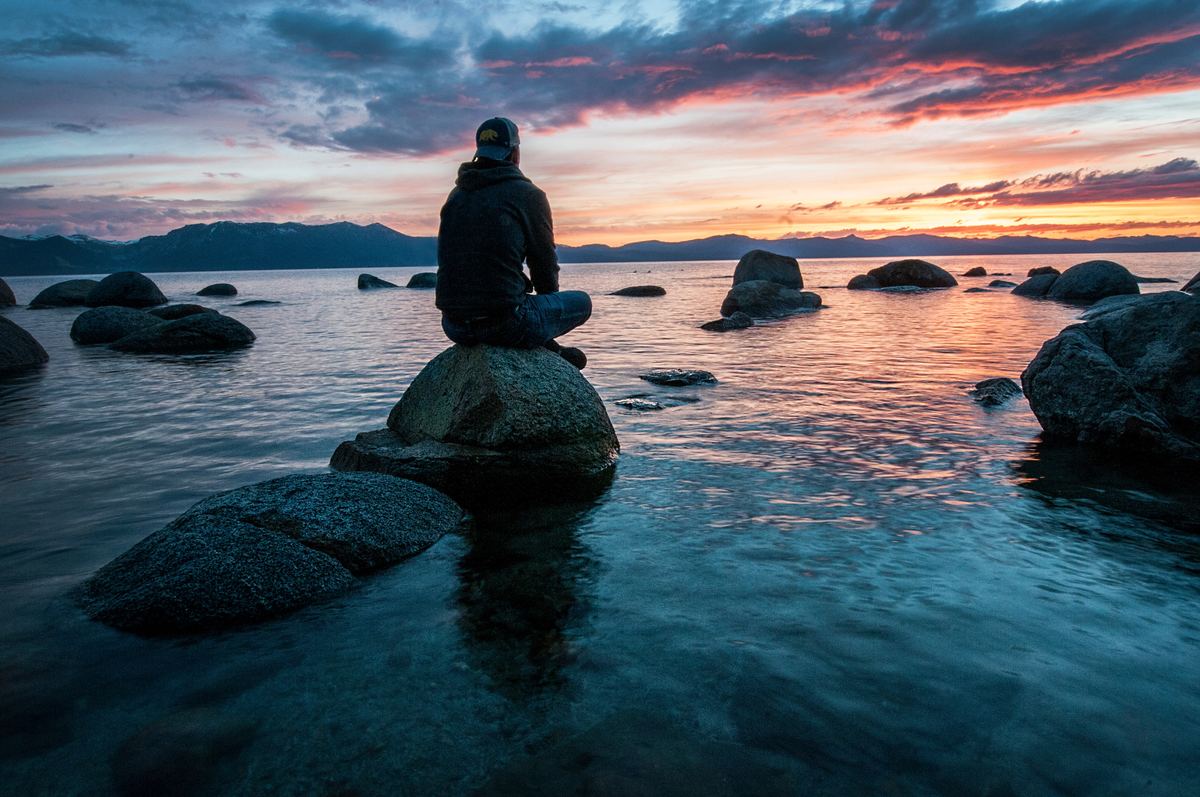 Person sitting alone on rock in water