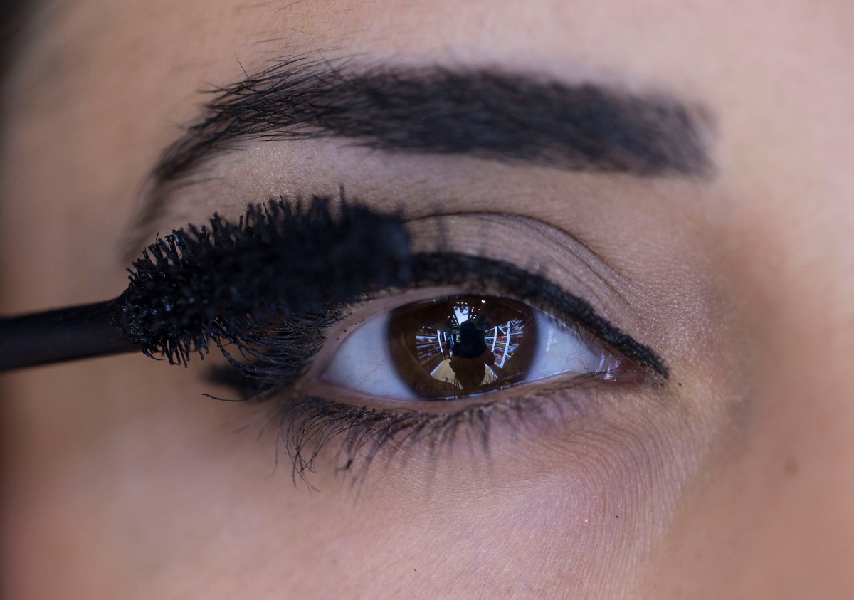Close-up shows a woman with brown eyes applying mascara.