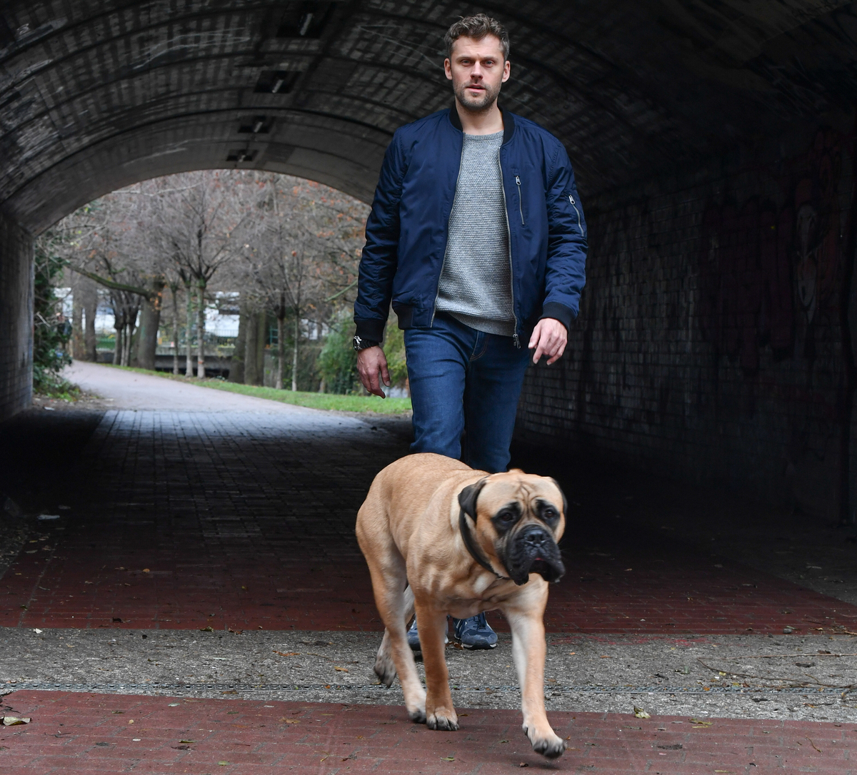 Actor Jens Atzorn walks with a bullmastiff through a tunnel.