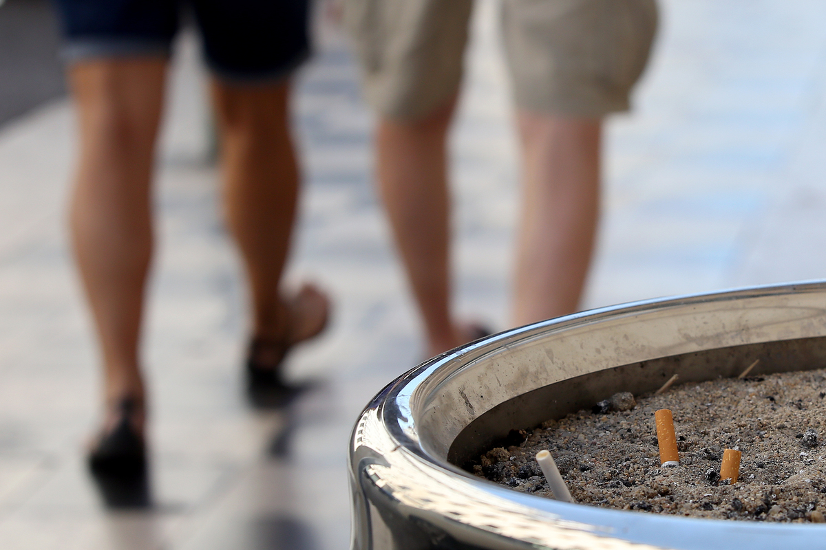 Two people walk away from a public ashtray.