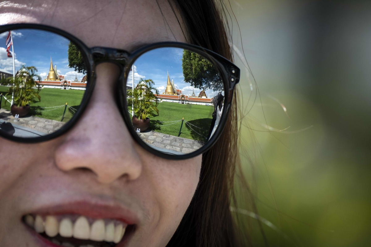 The Thai Royal Palace is reflected on the sunglasses of a tourist.