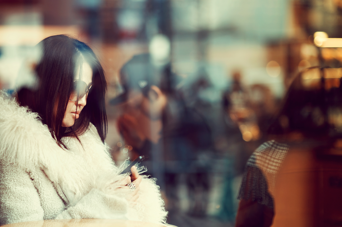 A fashionable young Japanese woman in sunglasses uses her mobile phone inside a cafe.