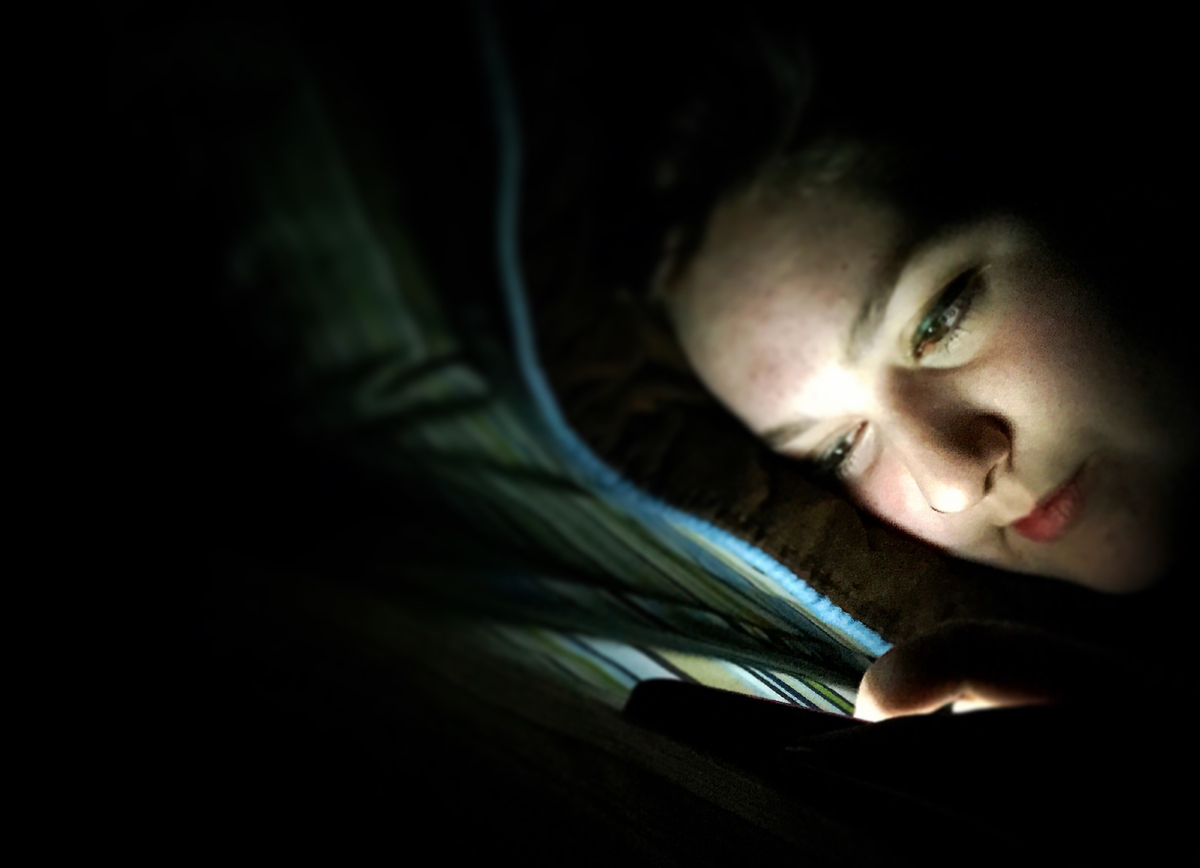 A teenage girl texts in her bed in the dark.