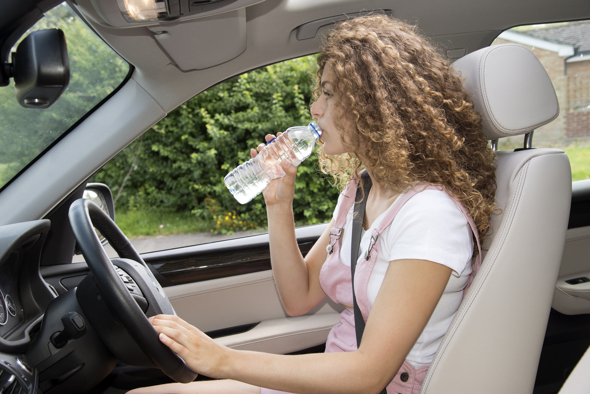A woman drinks from a water bottle while driving.