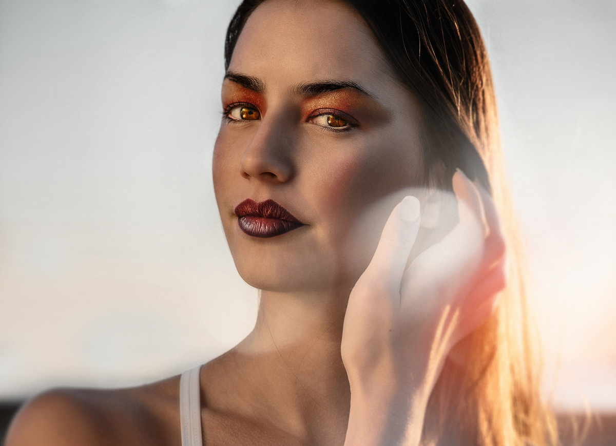 A woman with dramatic lipstick tucks her hair behind her ear.