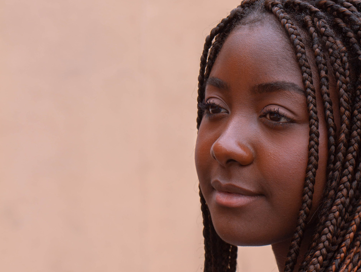 A woman looks into the distance in front of a peach-colored background.