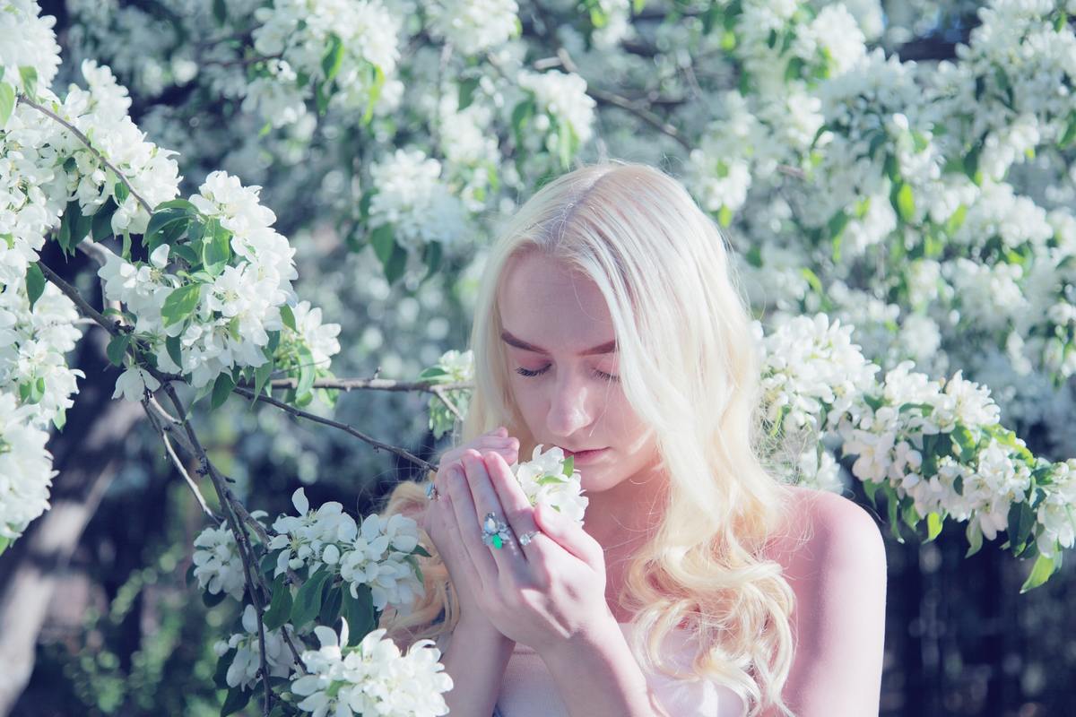 A teenager with glowing skin smells spring blossom flowers.