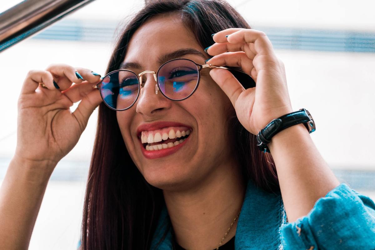 A woman smiles as she puts on her glasses.