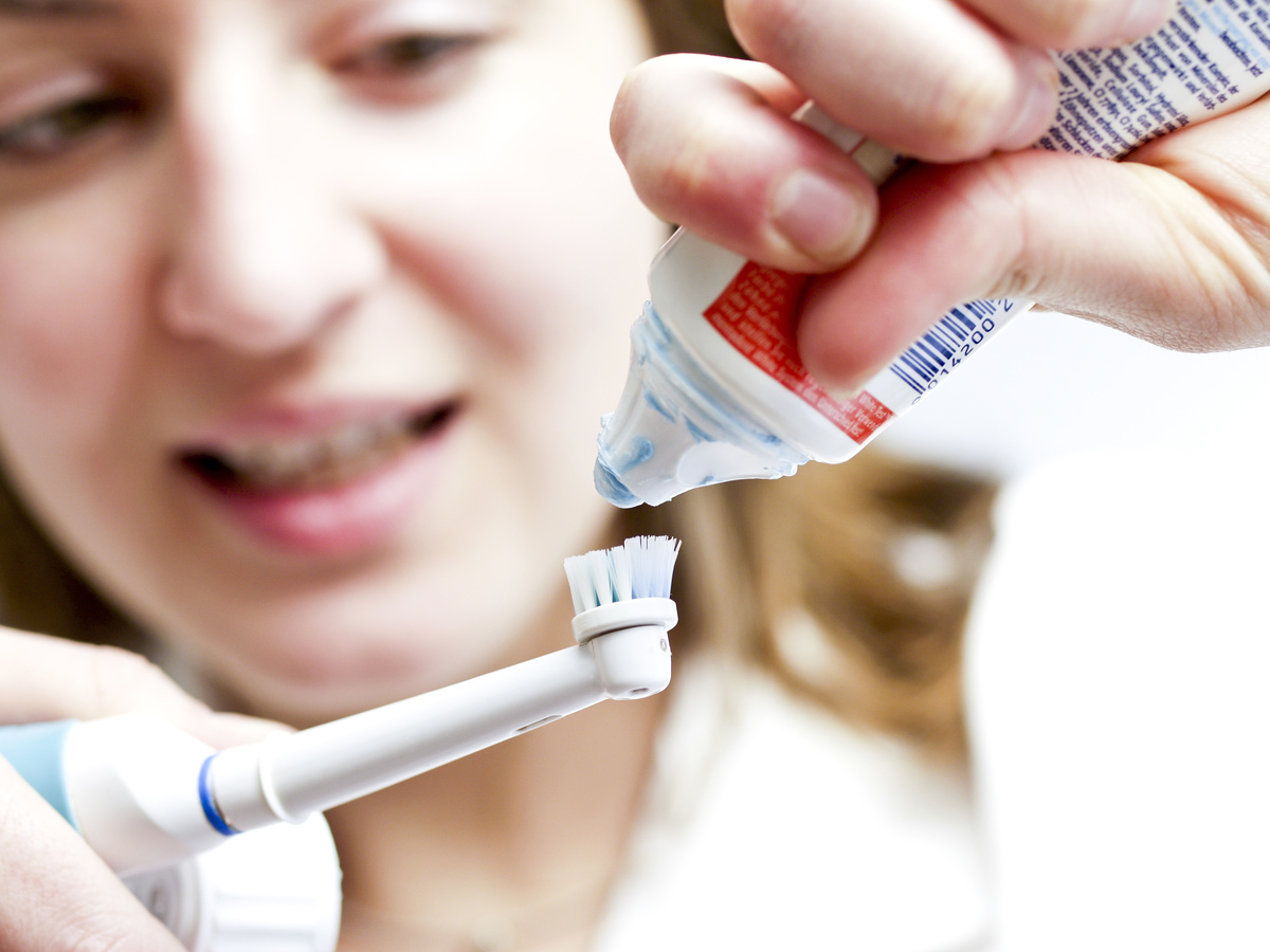 A woman applies toothpaste to an electric toothbrush.