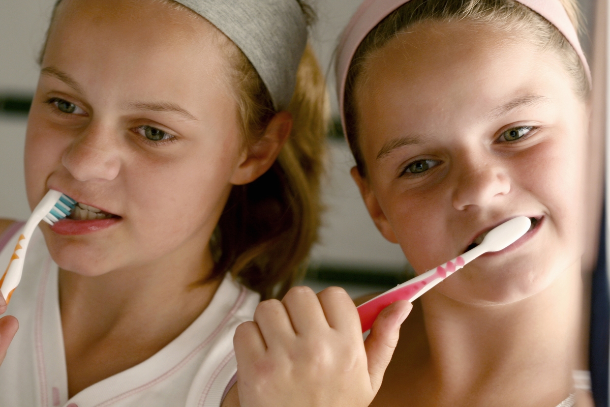 Two girls brush their teeth together.