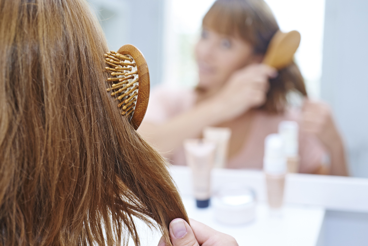 A woman brushes her hair while looking in a mirror.