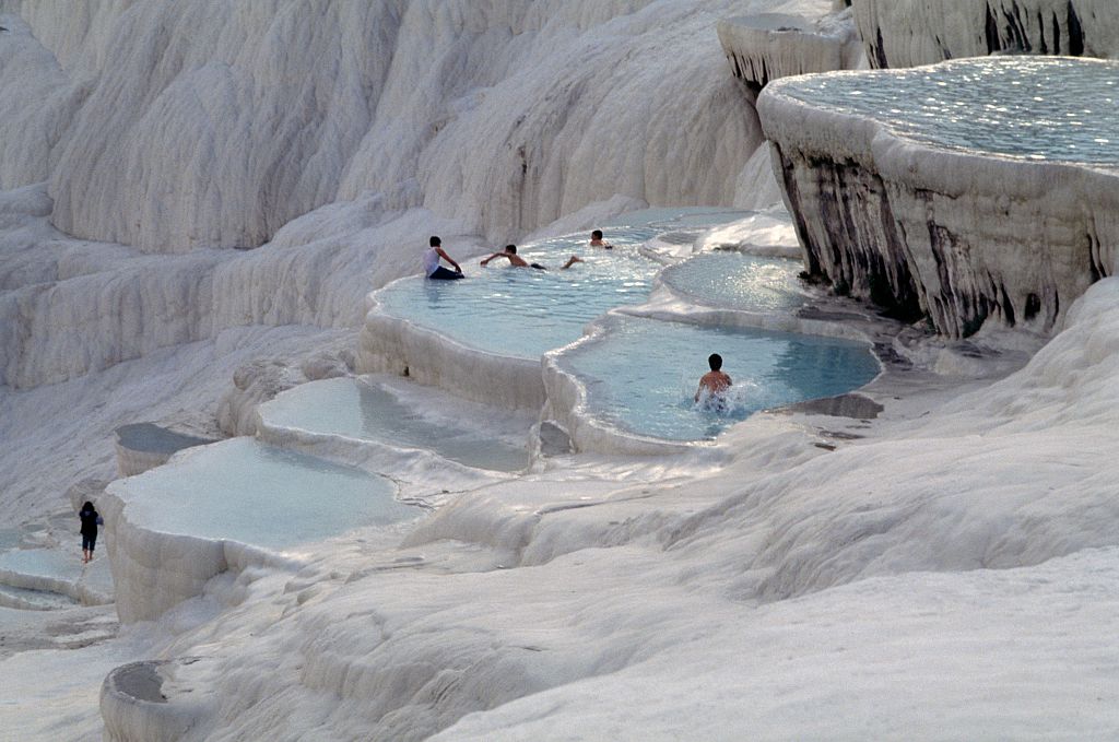 people swimming in the Pamukkale Thermal Pools along a white mountain