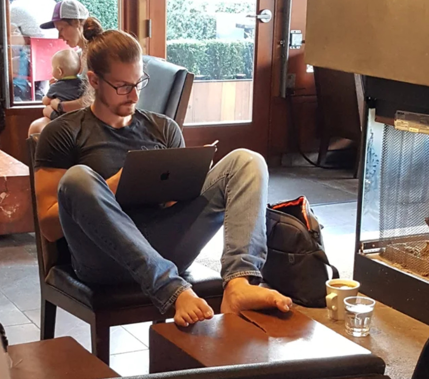 man takes shoes off and put his feet on a table in a coffee shop