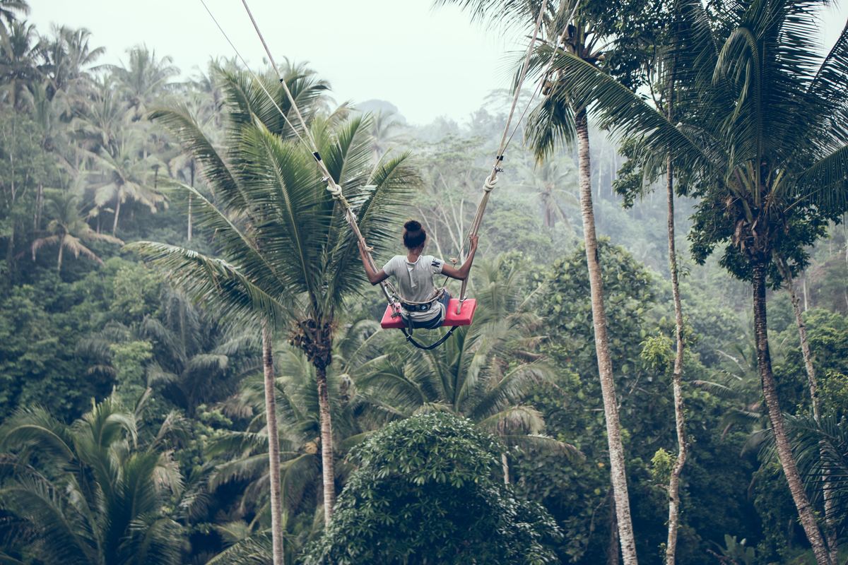 a girl swinging atop palm trees in bali