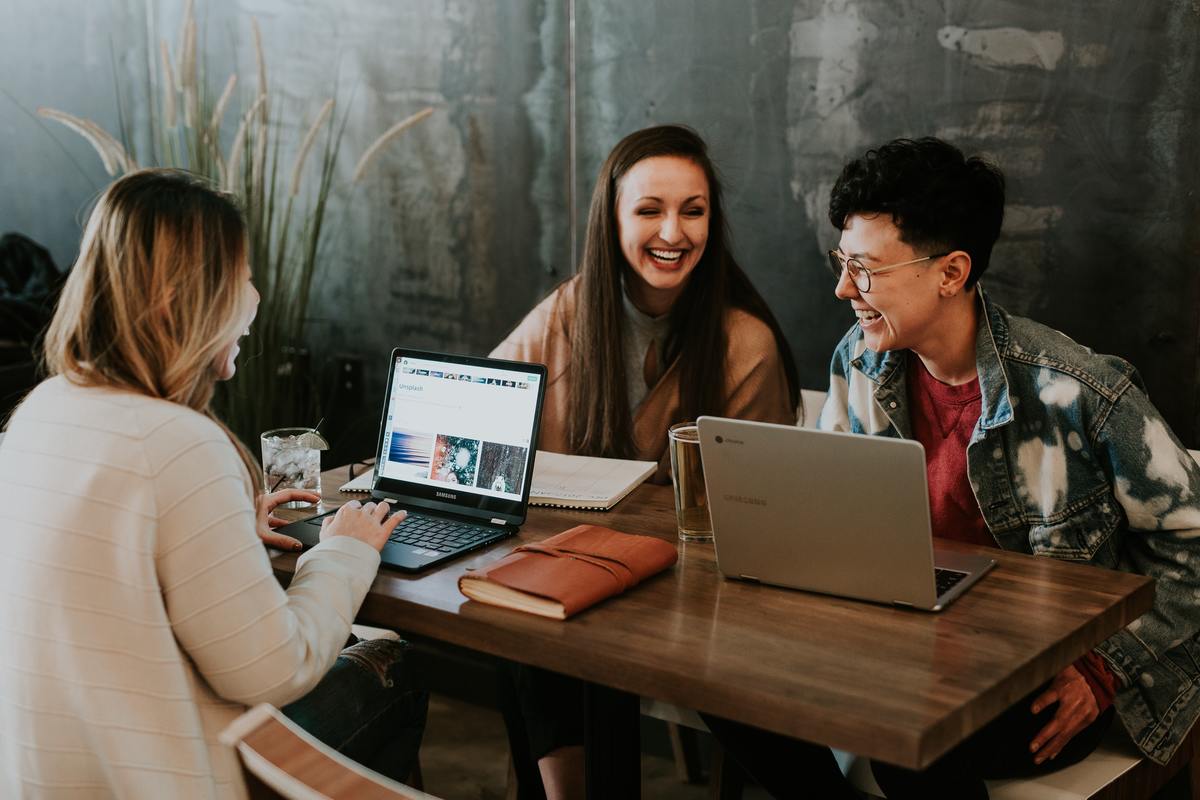 three women with laptops laughing at table