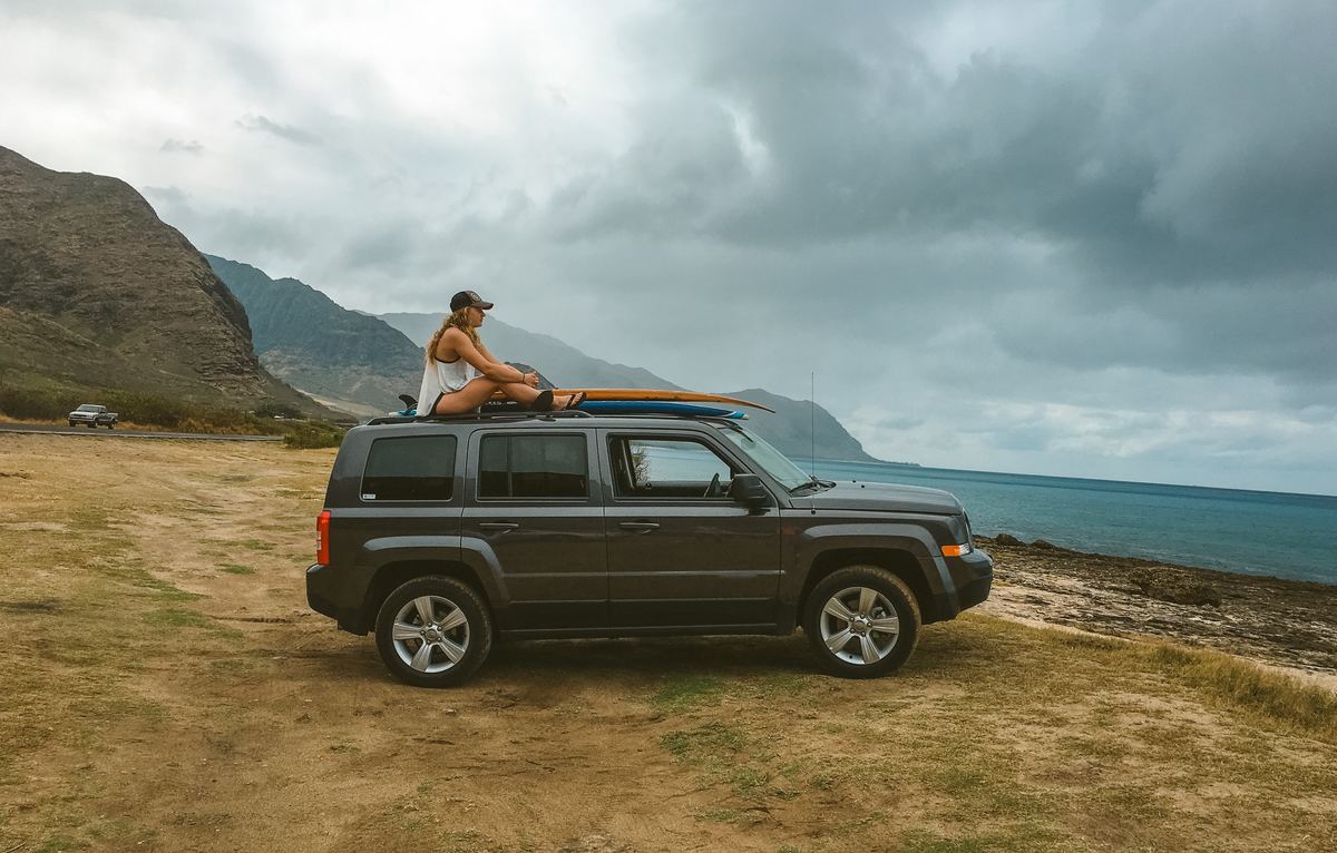 a girl sitting on top of a car on the beach in hawaii